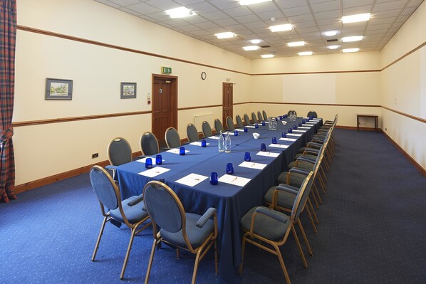 Un salón de conferencias con una larga mesa, sillas y botellas de agua.