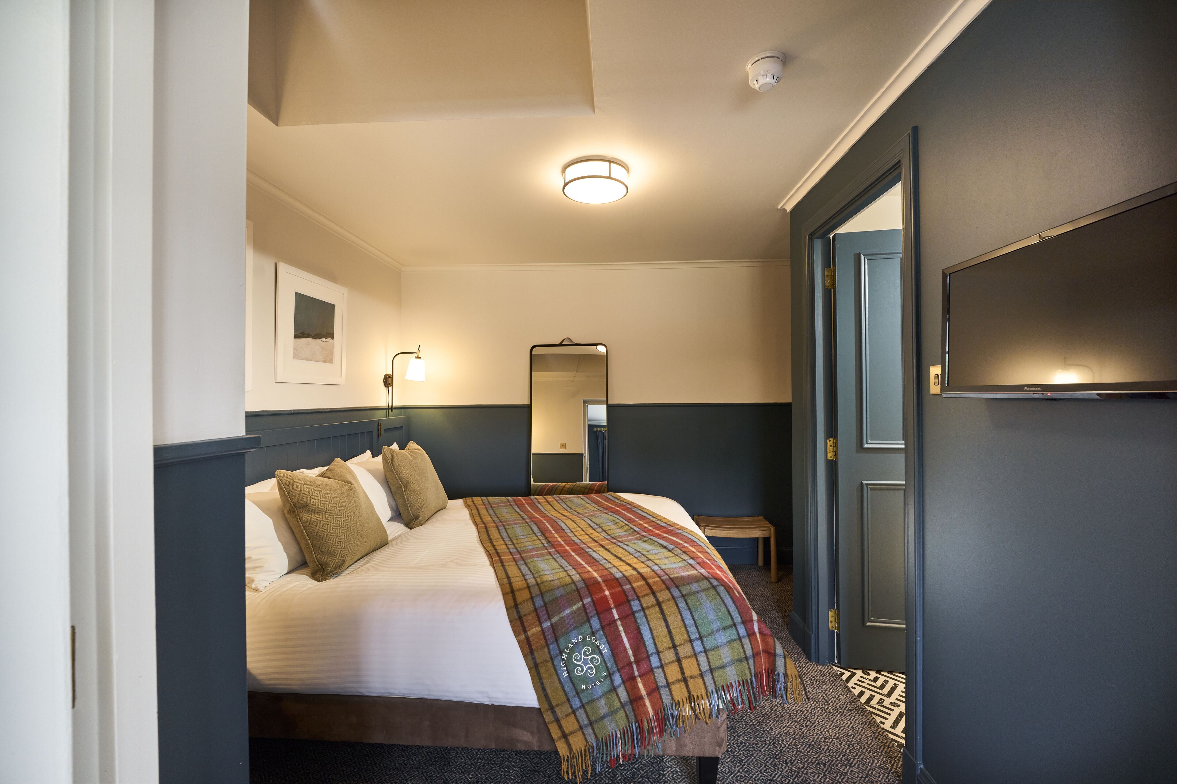 A hotel room with a bed, a bedside table, a mirror, and a TV.