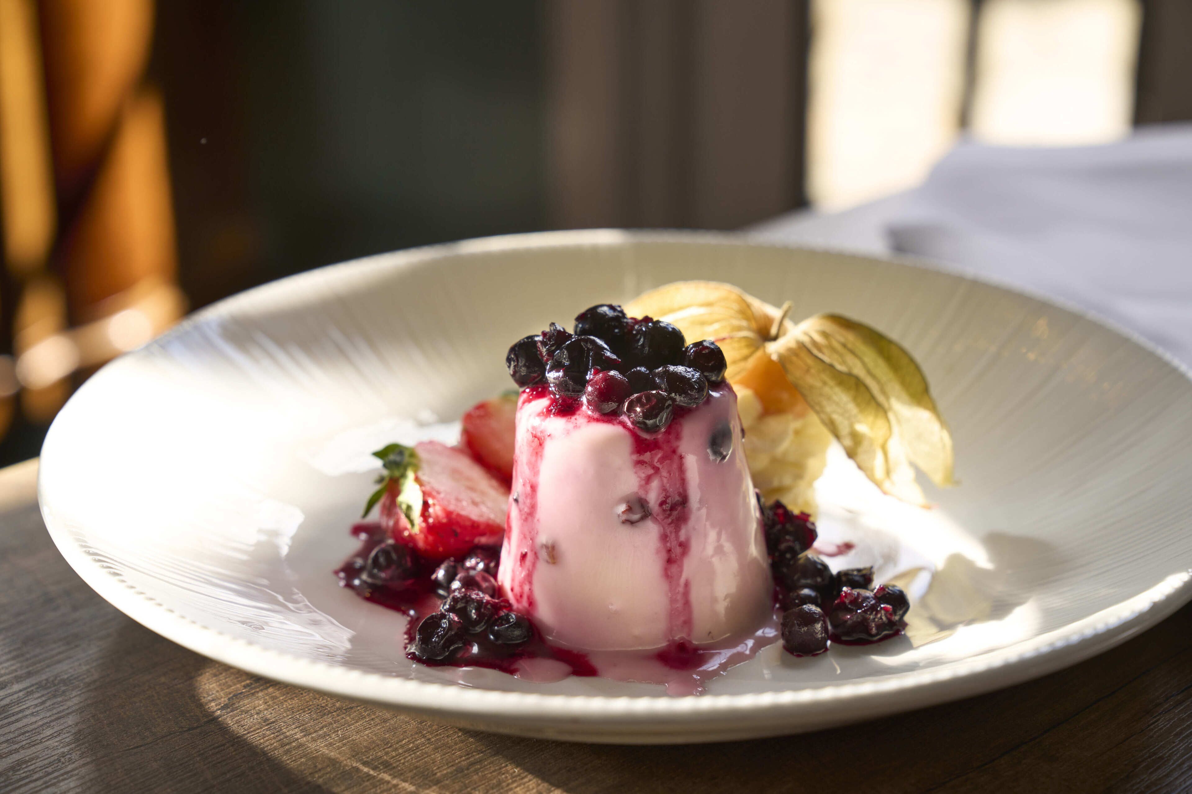 A dessert on a white plate with berries and a slice of cake.