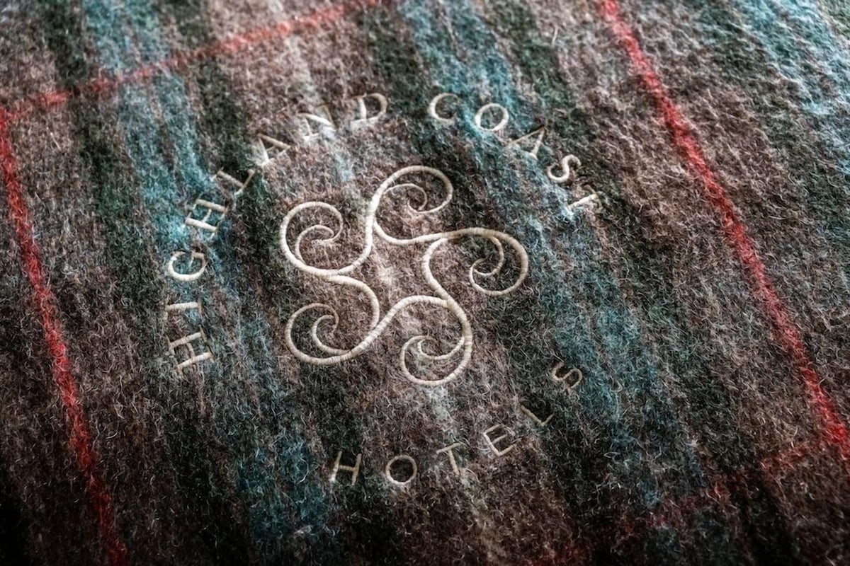 Tejido con texto bordado que dice 'HIGHLAND COAST HOTEL'.