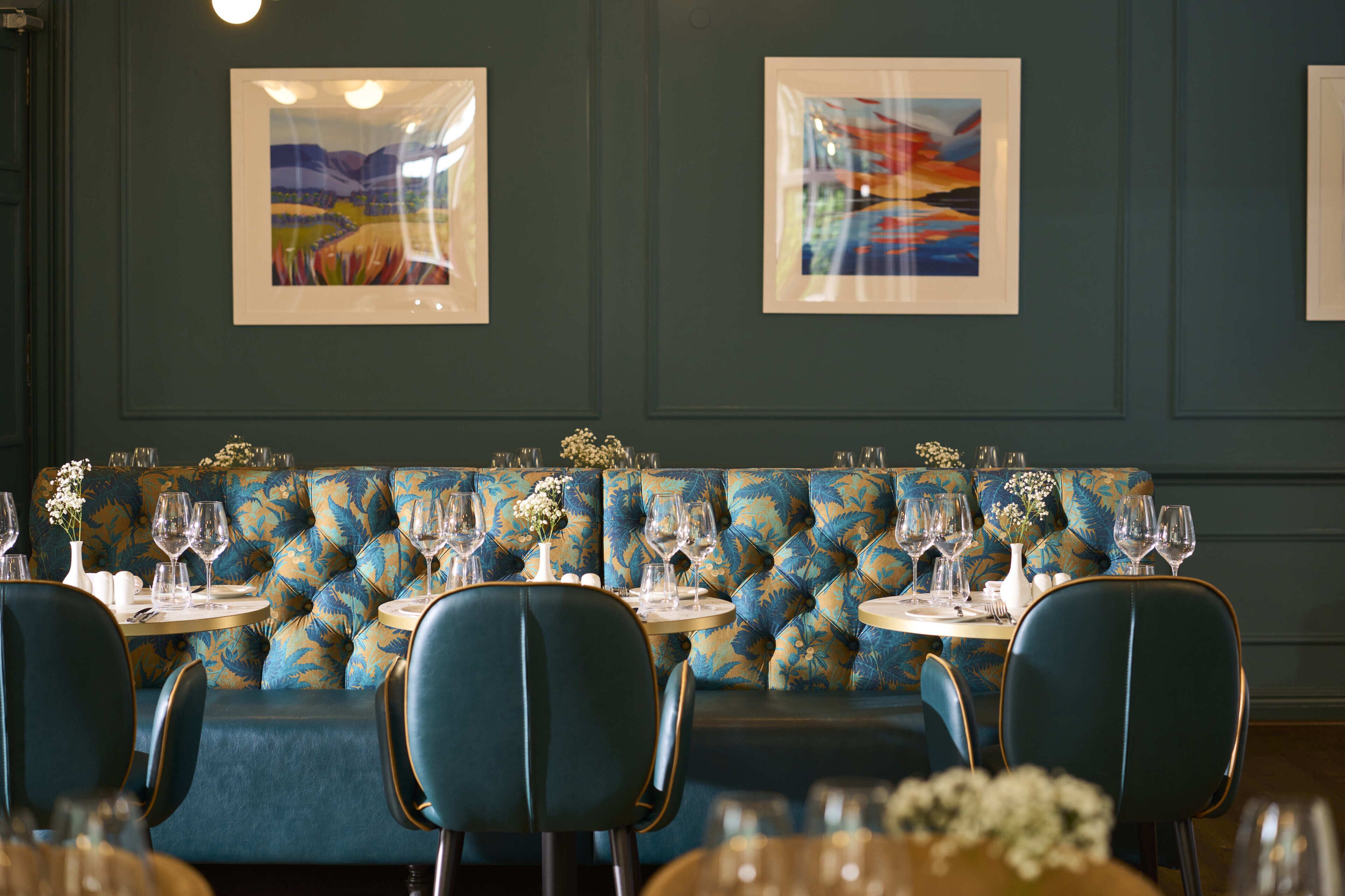 A restaurant with blue upholstered booths, round tables, and framed artwork on the walls.