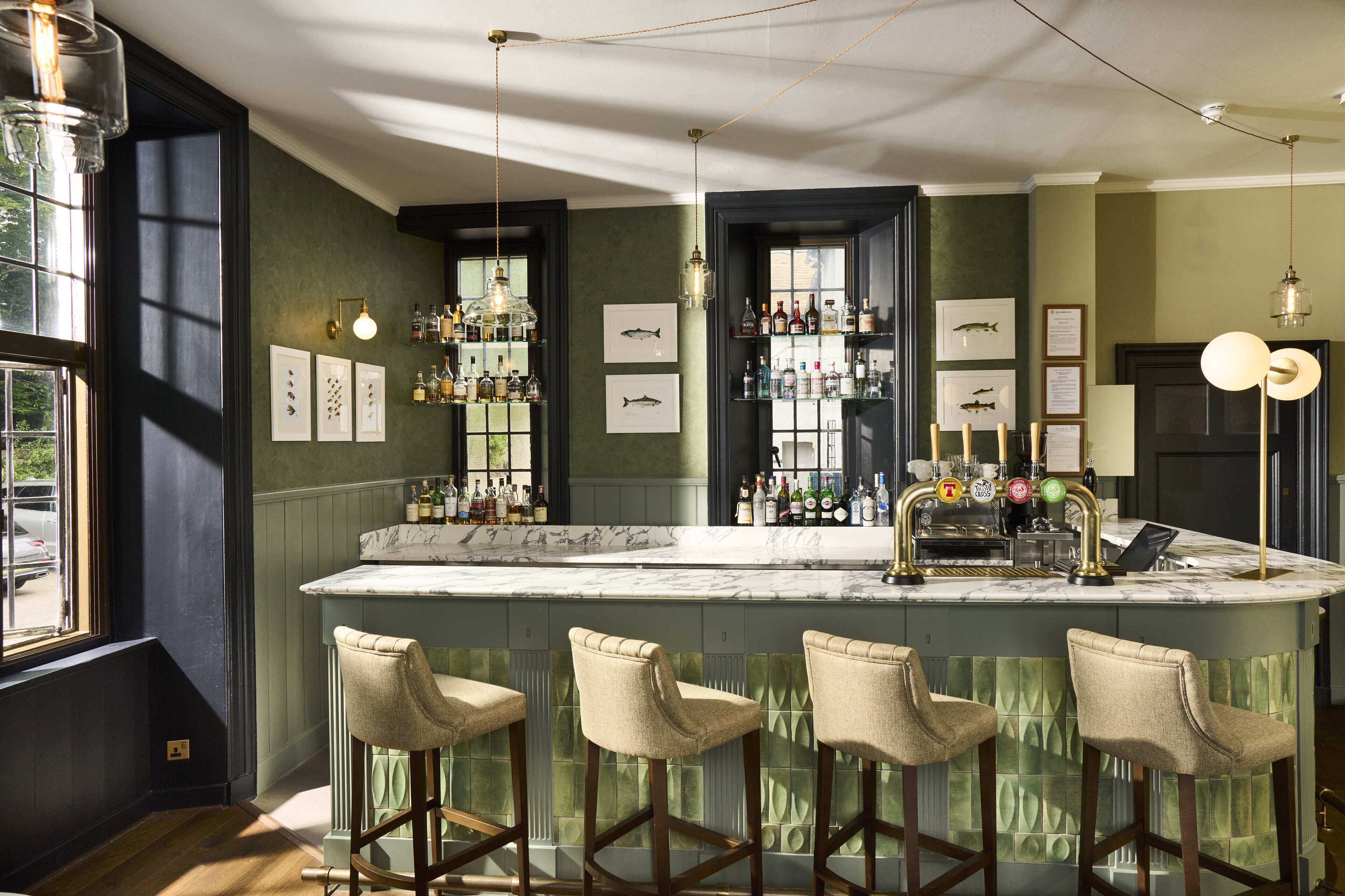 A bar area with a marble countertop, bar stools, hanging lights, and framed pictures on the walls.