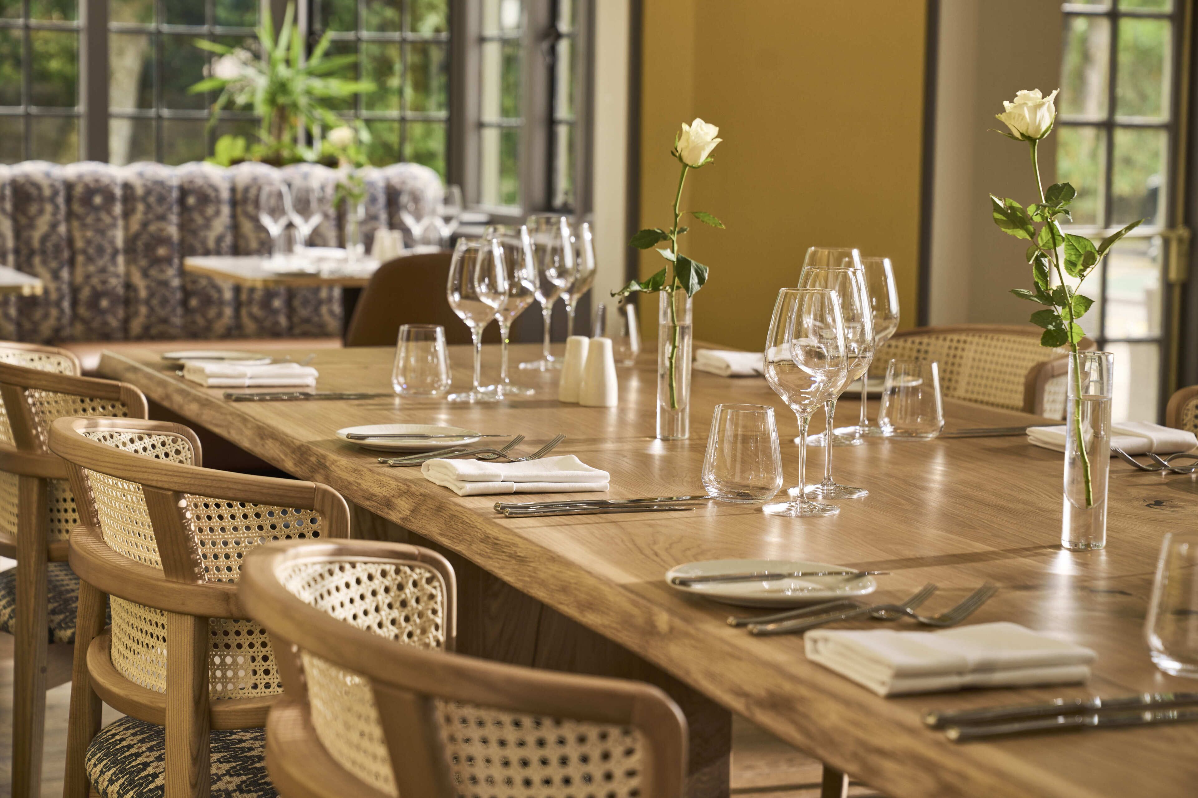 A dining table set with chairs, glasses, and a vase with a white rose.