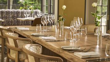 A dining table set with chairs, glasses, and a vase with a white rose.