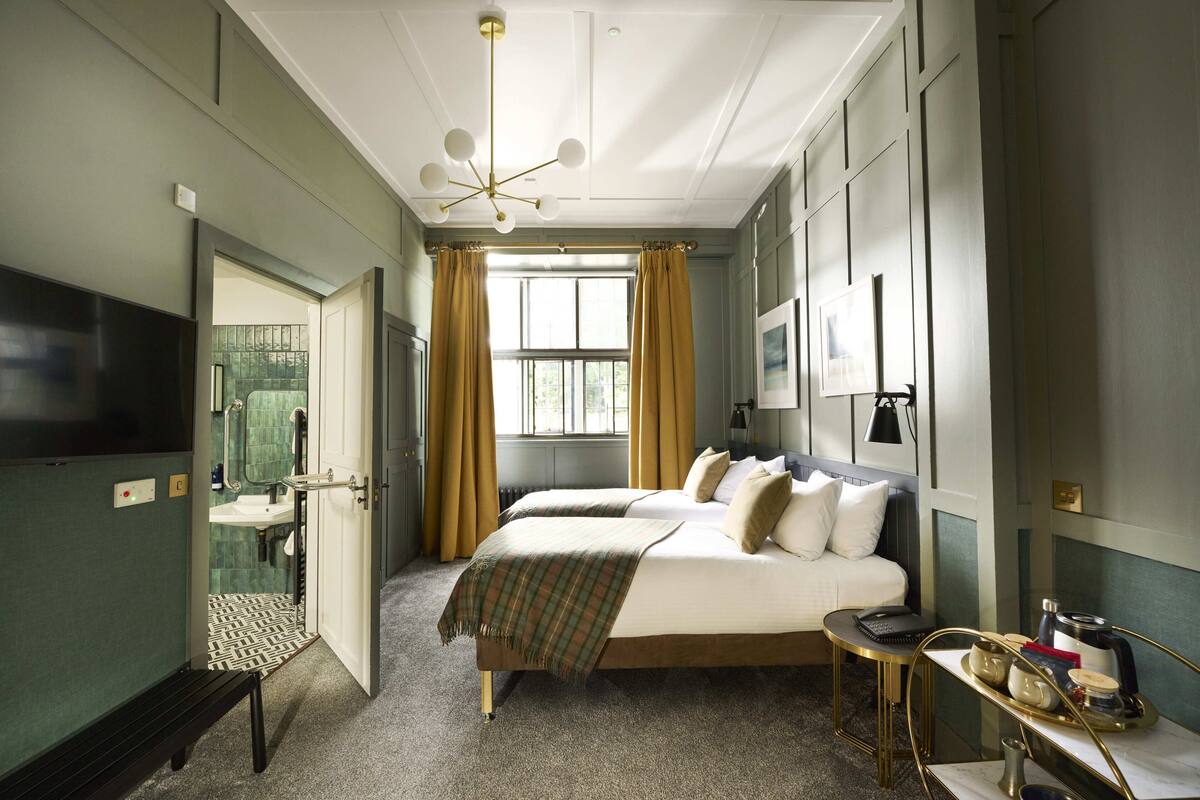 Ein Hotelzimmer mit Bett, Nachttisch und Blick durch ein Fenster nach draußen.