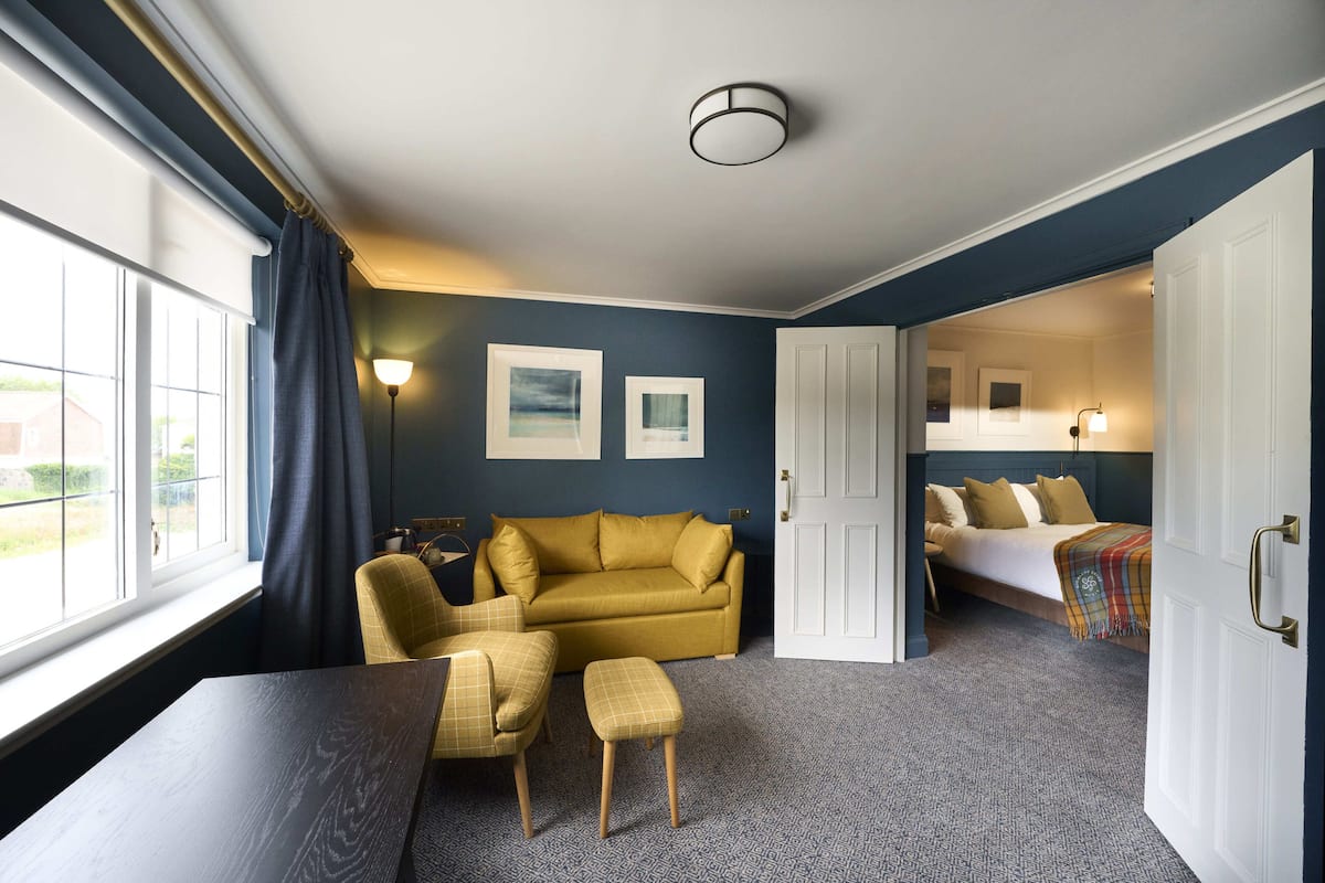 Ein Hotelzimmer mit Sofa, kleinem Tisch, Stuhl, Bett und einer Tür zu einem weiteren Raum.