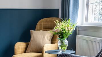 Un rincón acogedor con un sillón a cuadros, un sillón estampado y una mesita con un jarrón de flores.