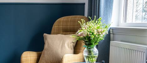 A cozy seating area with a checkered armchair, a patterned armchair, and a small table with a vase of flowers.