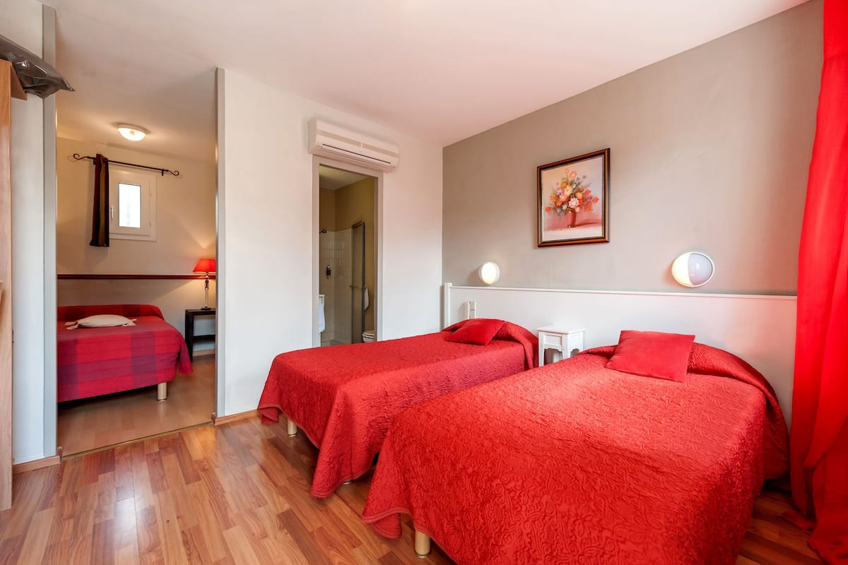 Une chambre d’hôtel avec deux lits simples, une petite table, une lampe et un espace douche.