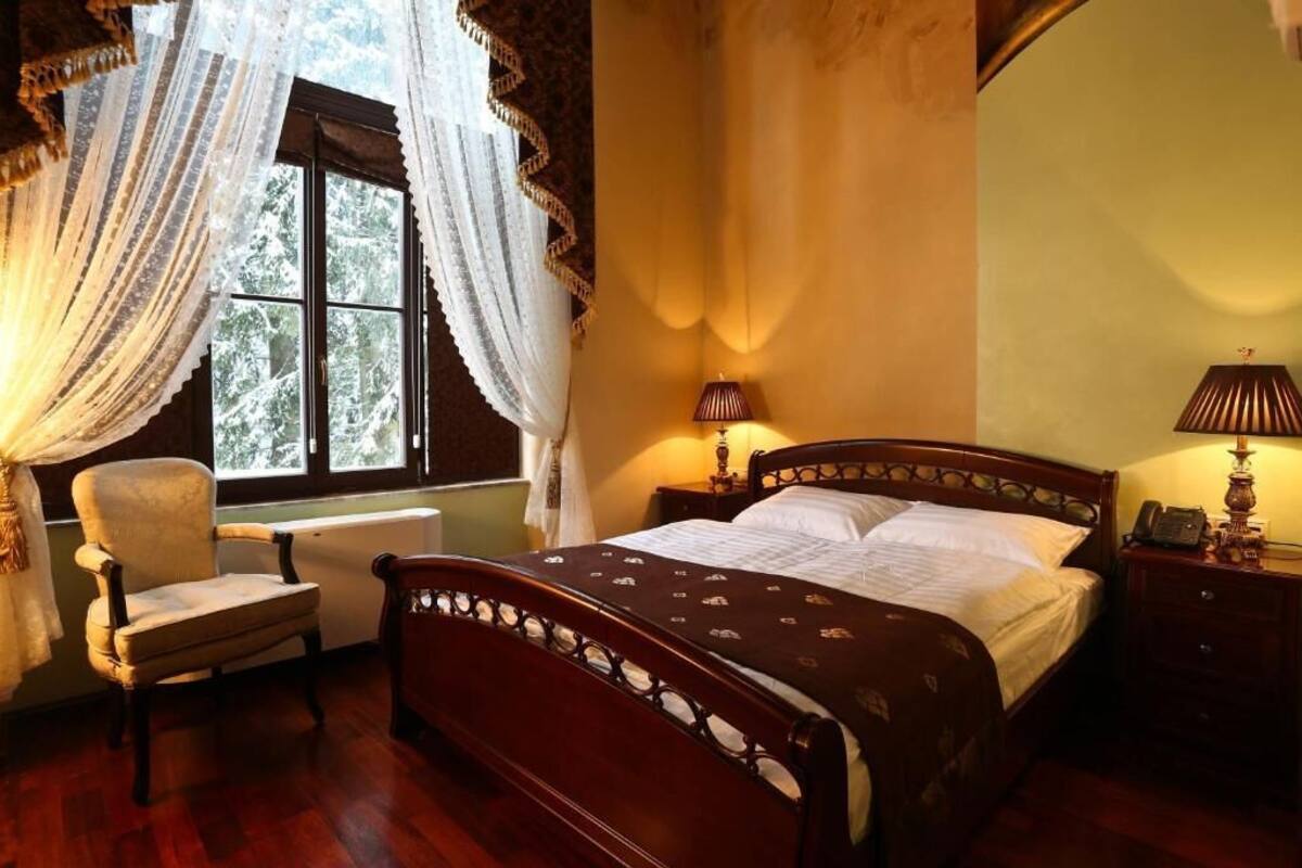 A bedroom with a wooden bed, a chair, a nightstand, and a window with curtains.