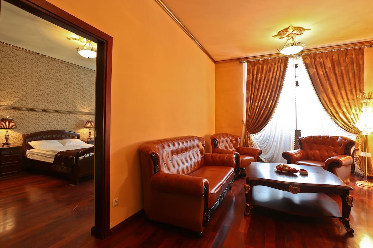 A room with a bed, a brown leather sofa, a wooden coffee table, and a chair.