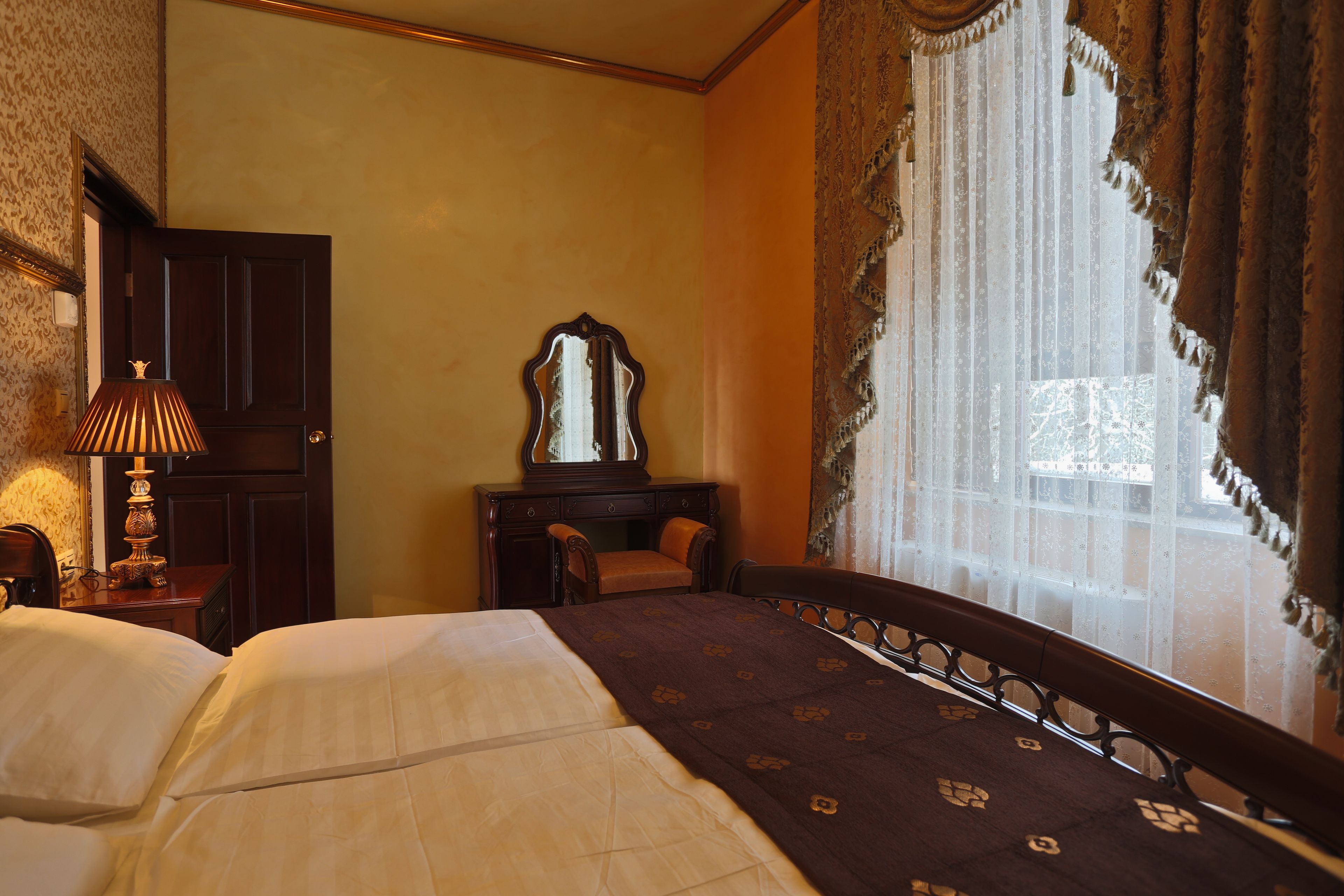 A hotel room with a bed, a desk, a chair, a lamp, and a window with curtains.