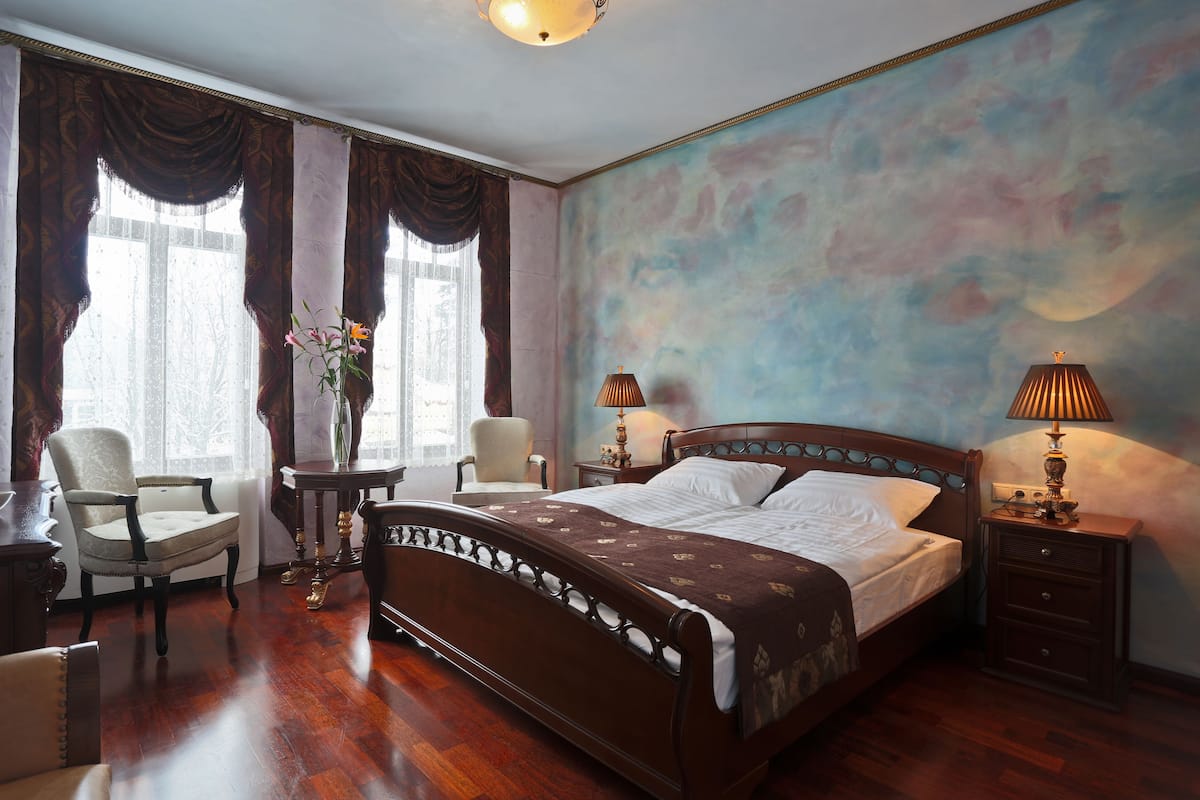 A bedroom with a large bed, two bedside tables with lamps, a chair, and a desk.