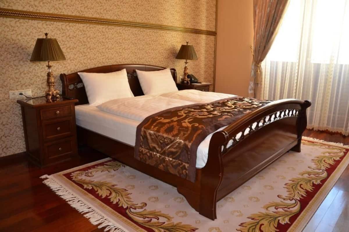 A neatly made bed with a patterned bedspread, two bedside tables with lamps, a wooden headboard, and a decorative rug.