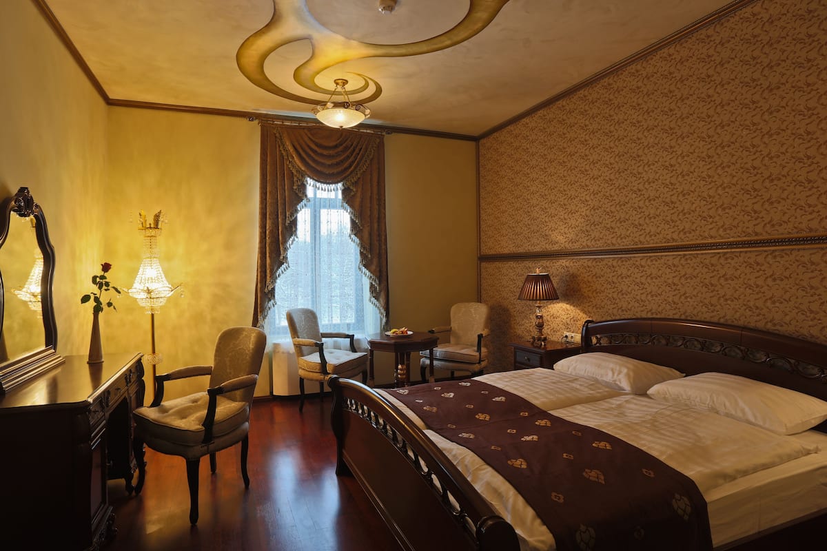 A hotel room with a large bed, two chairs, a desk, and a lamp.