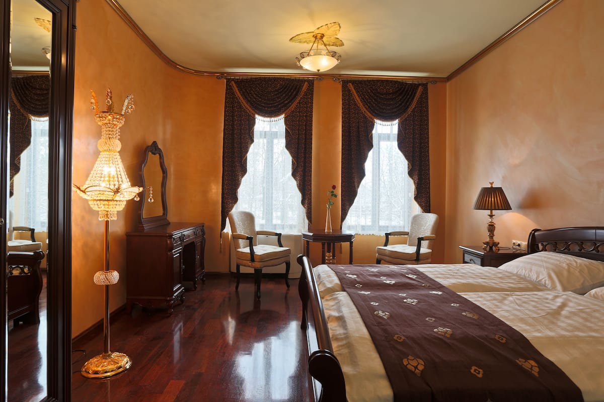 A hotel room with a large bed, two chairs, a table, a mirror, and a chandelier.