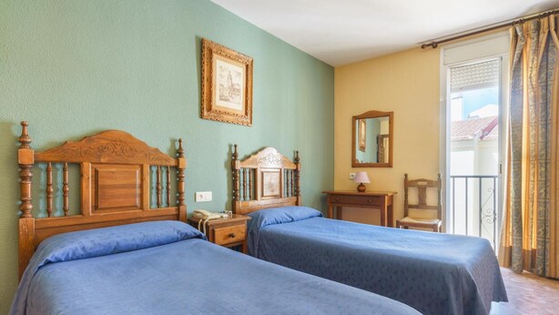 A room with two wooden beds, a small table with a lamp, a chair, and a balcony with curtains. - Arunda I (Ronda)