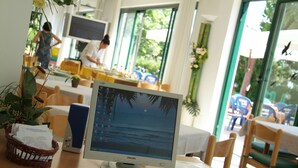 Un computer desktop con schermo che mostra una spiaggia, posizionato su un tavolo di legno in una stanza con ampie finestre e vista sull'esterno.