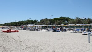 Una spiaggia con file di lettini e ombrelloni, una barca rossa e un cielo sereno.