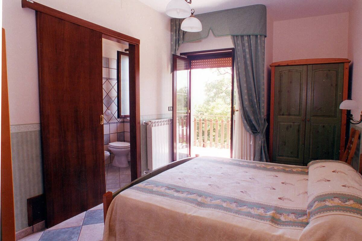 Ein Schlafzimmer mit Bett, einem Holzschrank, einem Badezimmer mit Toilette und einem Balkon mit Aussicht.