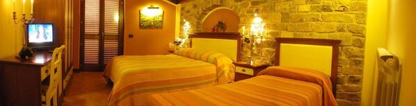 A hotel room with two beds, a television, a desk, and a stone wall.