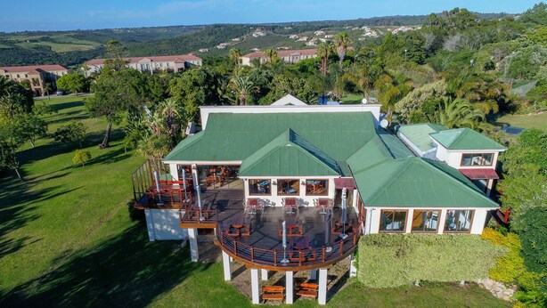 A large, multi-story house with a green roof, a circular deck with outdoor furniture, and a well-maintained lawn. - Castleton (Plettenberg Bay)