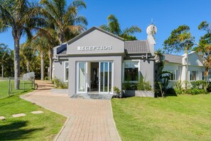 A reception building with a clear entrance, surrounded by palm trees and a well-maintained lawn. - Castleton (Plettenberg Bay)