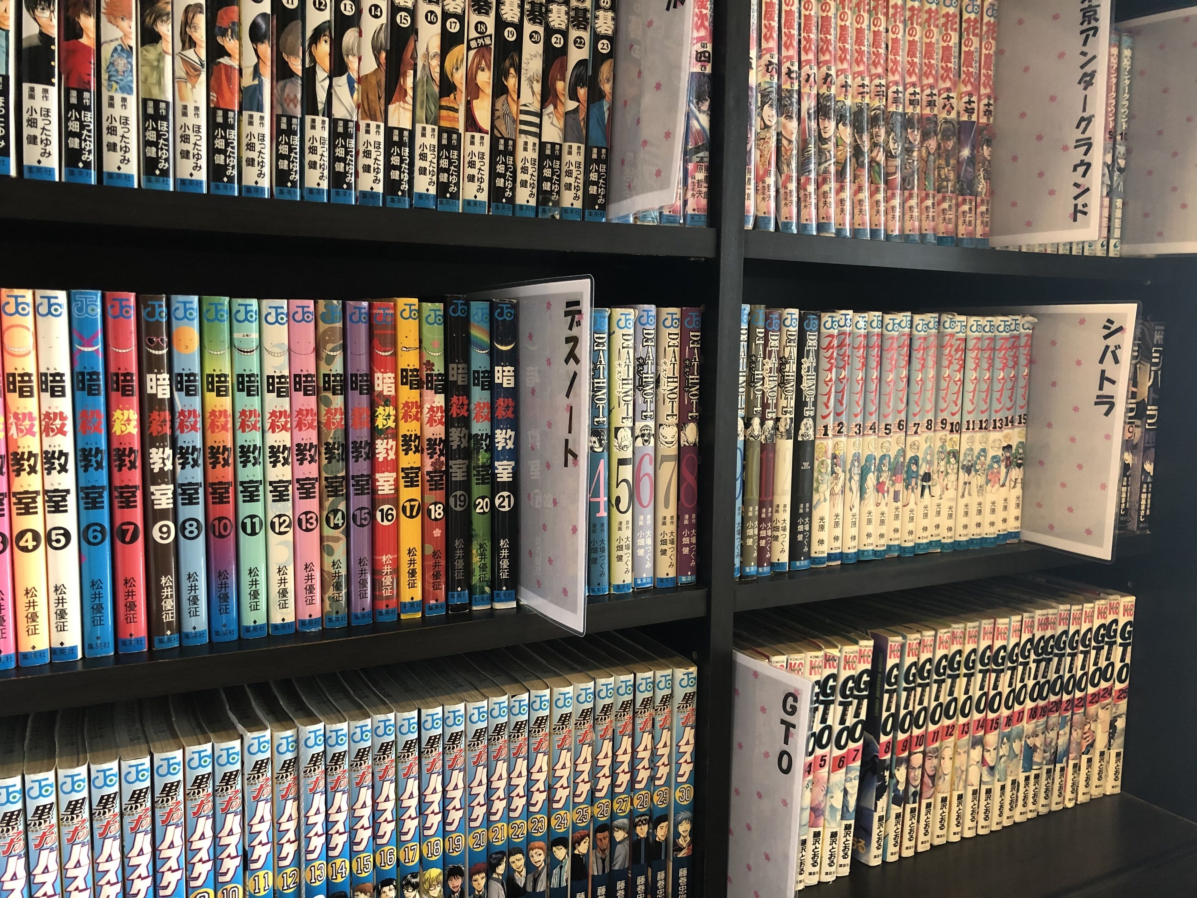 A bookshelf filled with manga volumes, organized by series and volume numbers.