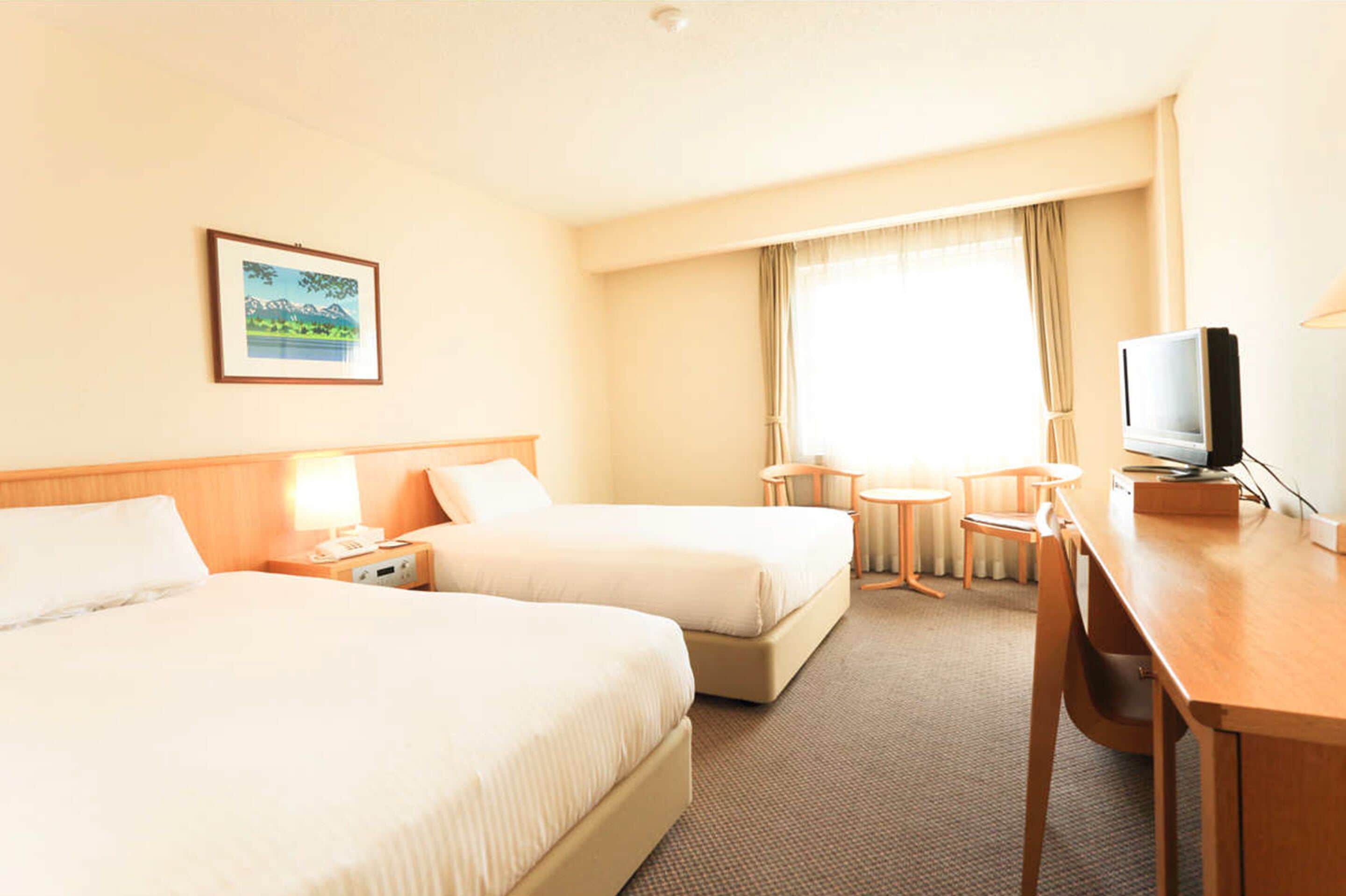 A hotel room with two beds, a desk, a chair, a television, and a window with curtains.