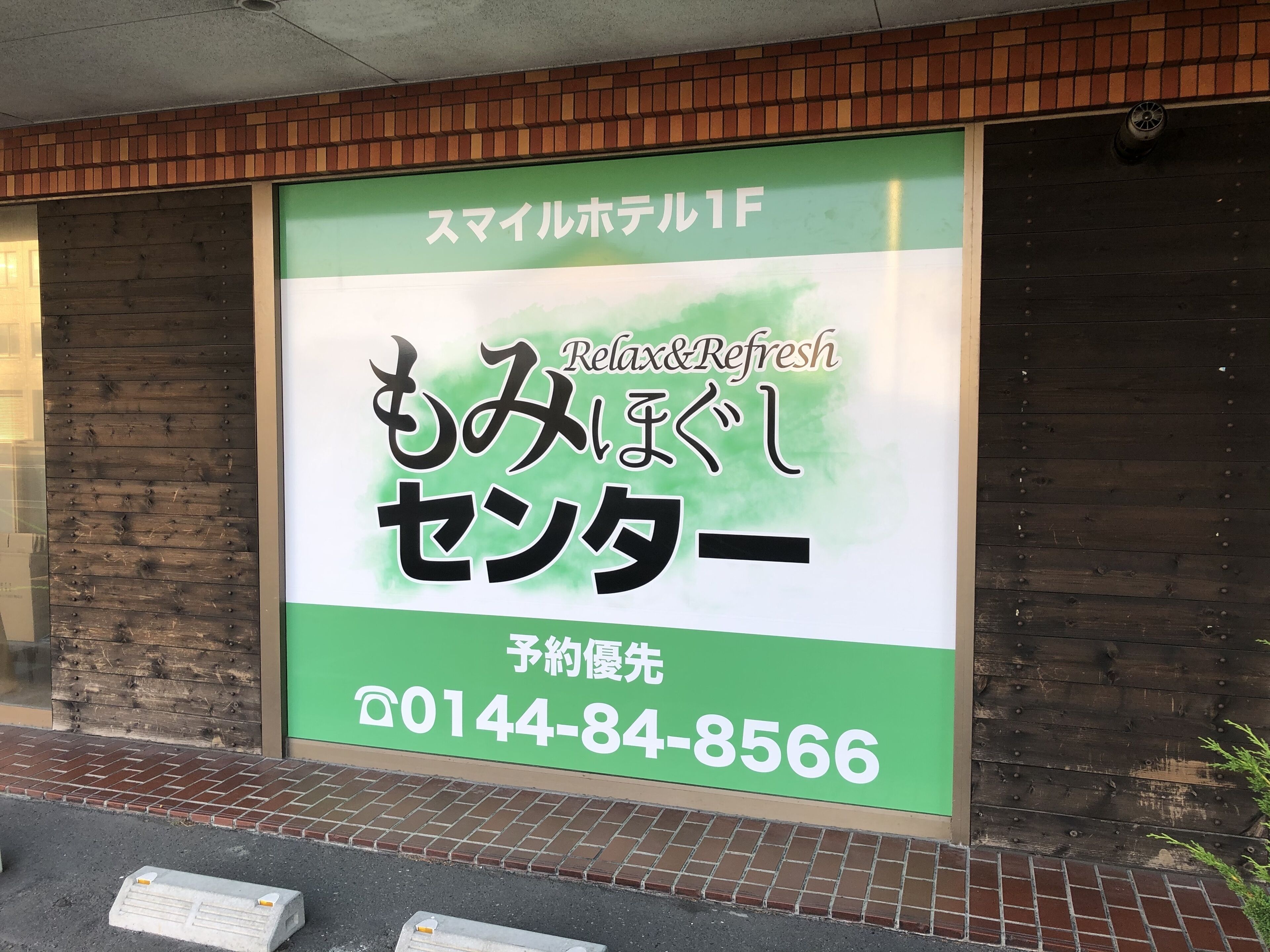 Un cartel grande anuncia un hotel con el tema Relájate y Recárgate, mostrando texto en japonés y un número de contacto.