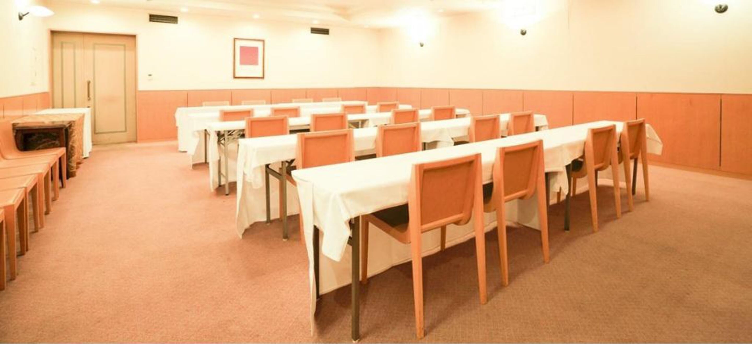Une salle de conférence avec plusieurs tables et chaises, un sol recouvert de moquette et une porte au fond.