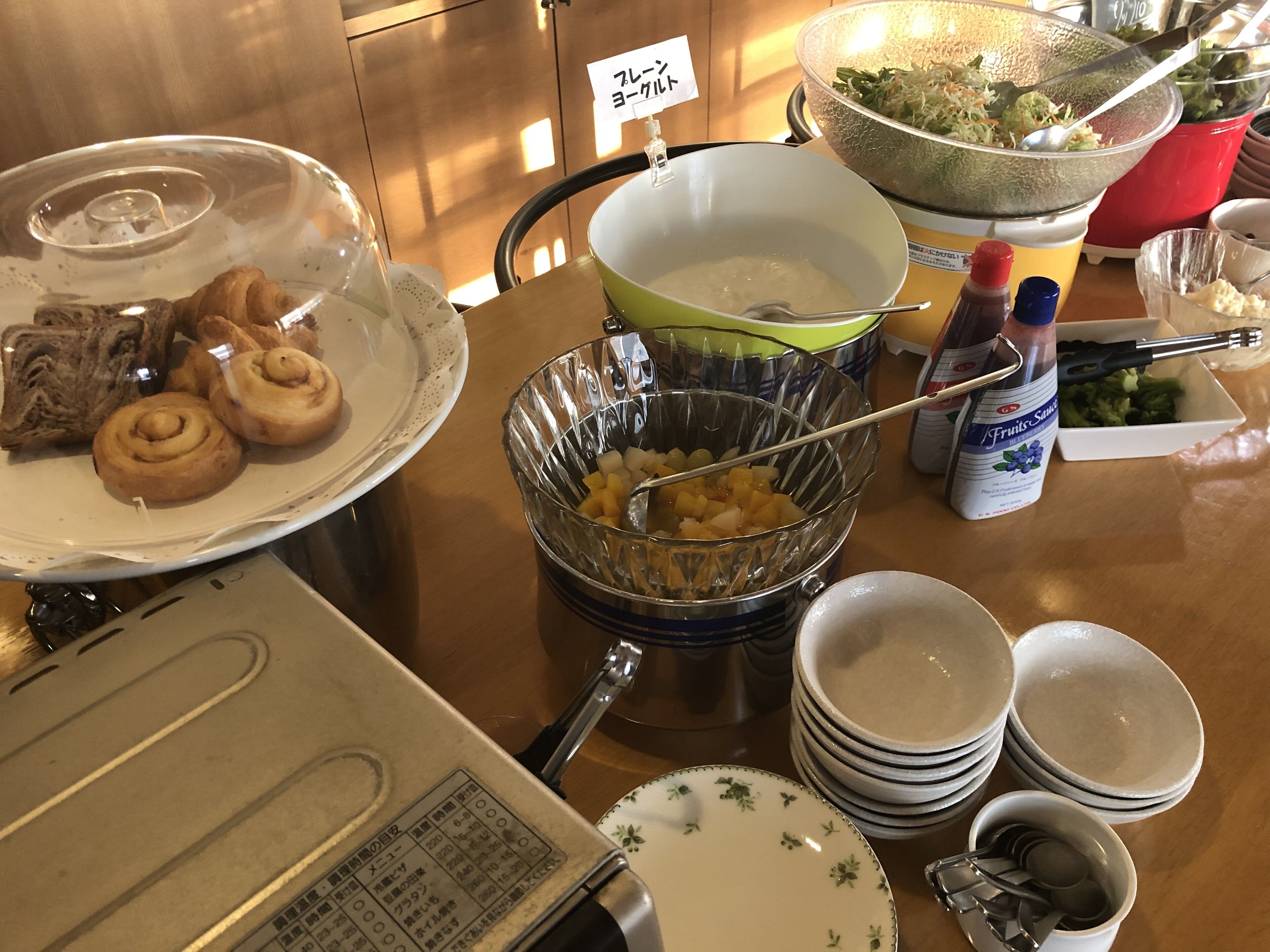 Una mesa de buffet con diversos alimentos, como pasteles, un bol de fruta y salsas.