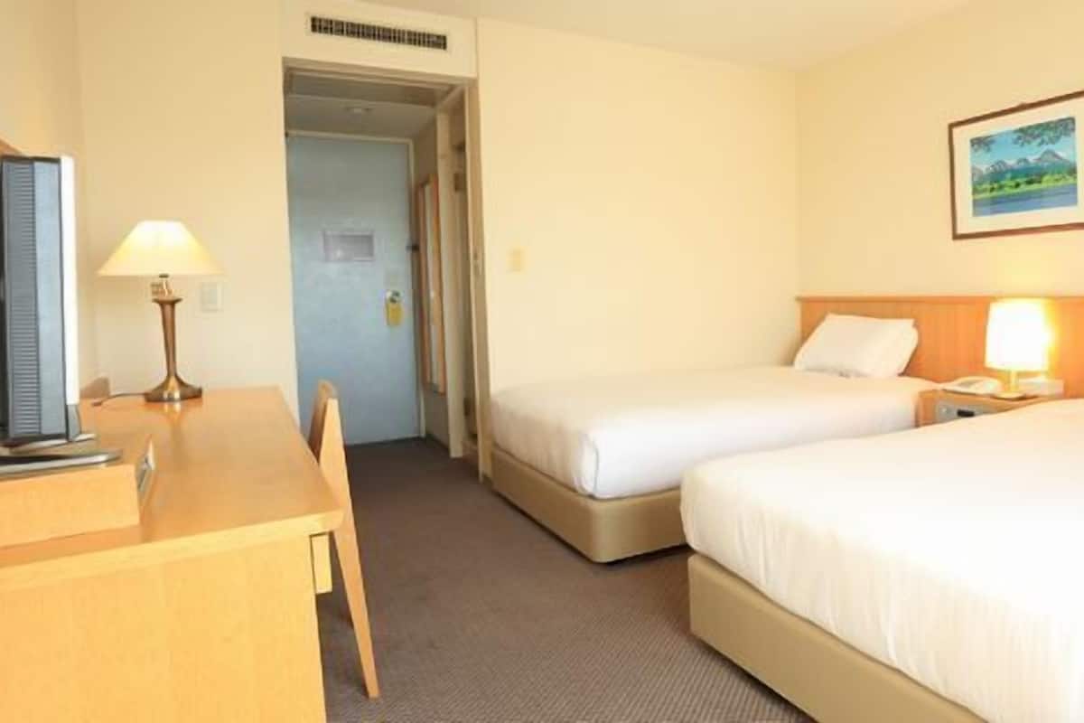 Ein Hotelzimmer mit zwei Betten, einem Schreibtisch, einer Lampe und einem Gemälde an der Wand.