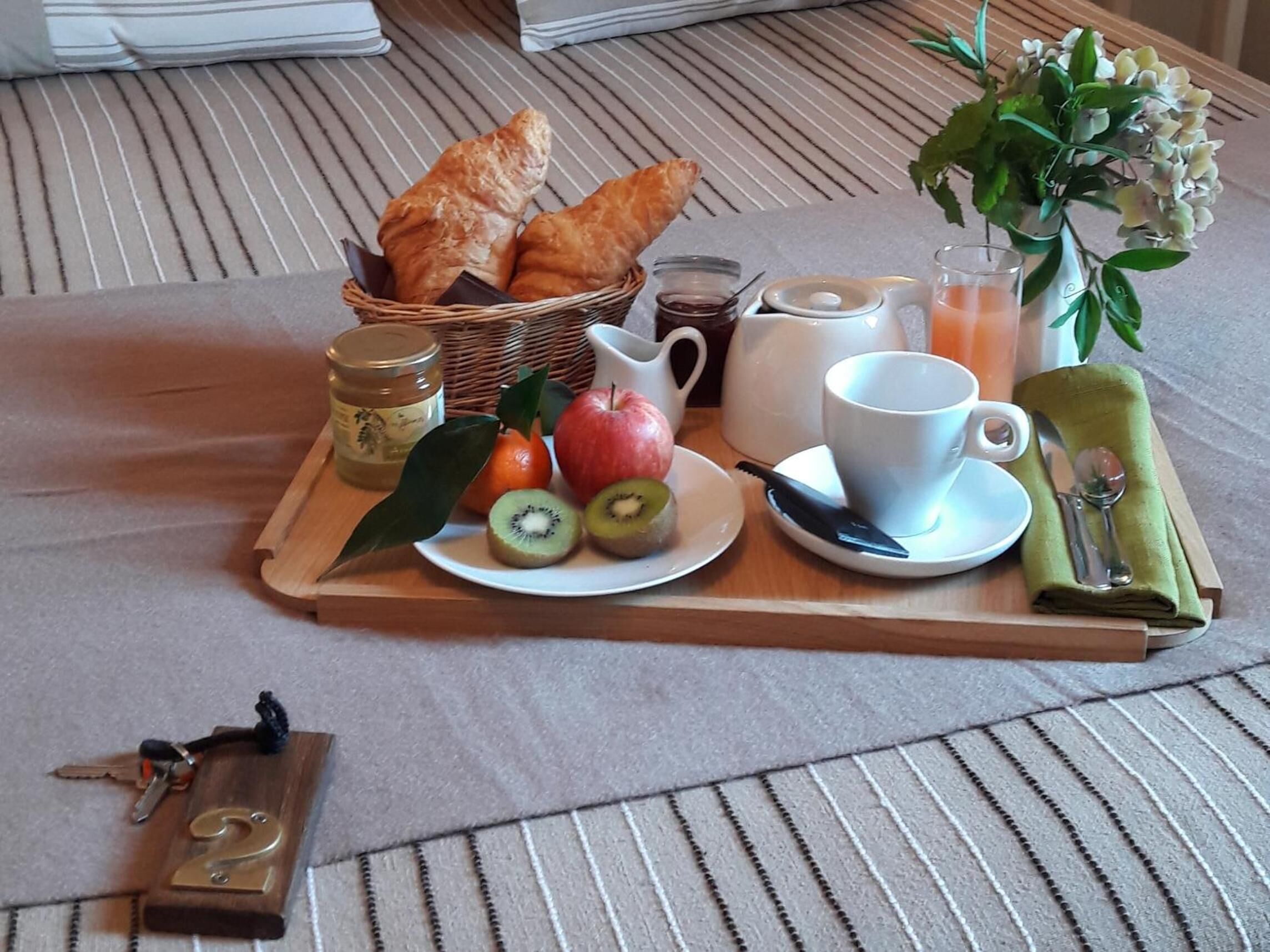 Una bandeja de desayuno con cruasanes, frutas, una taza y un florero con flores sobre una cama.