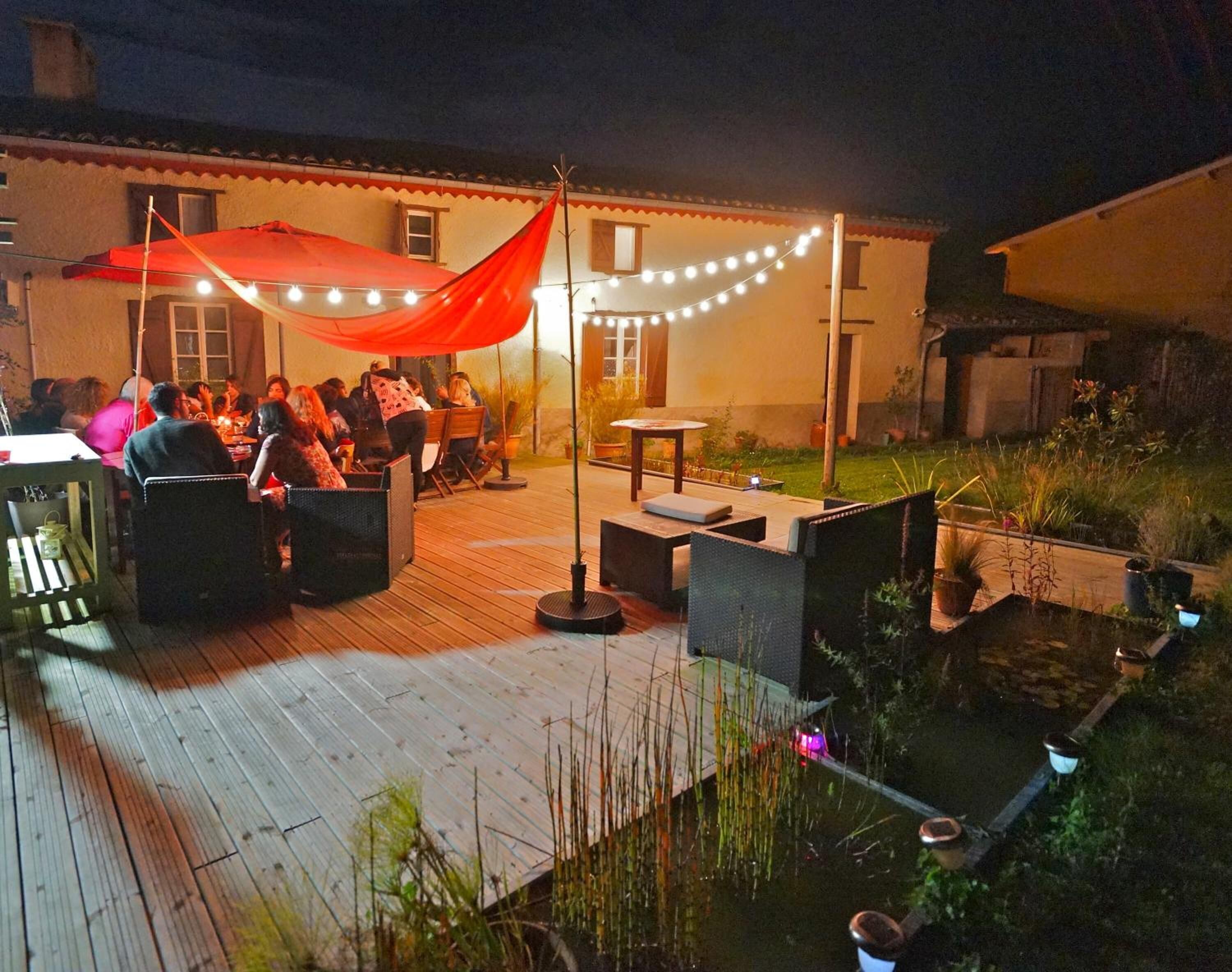 Un espace extérieur aménagé pour les repas, avec des tables et des chaises, une terrasse en bois et des guirlandes lumineuses.