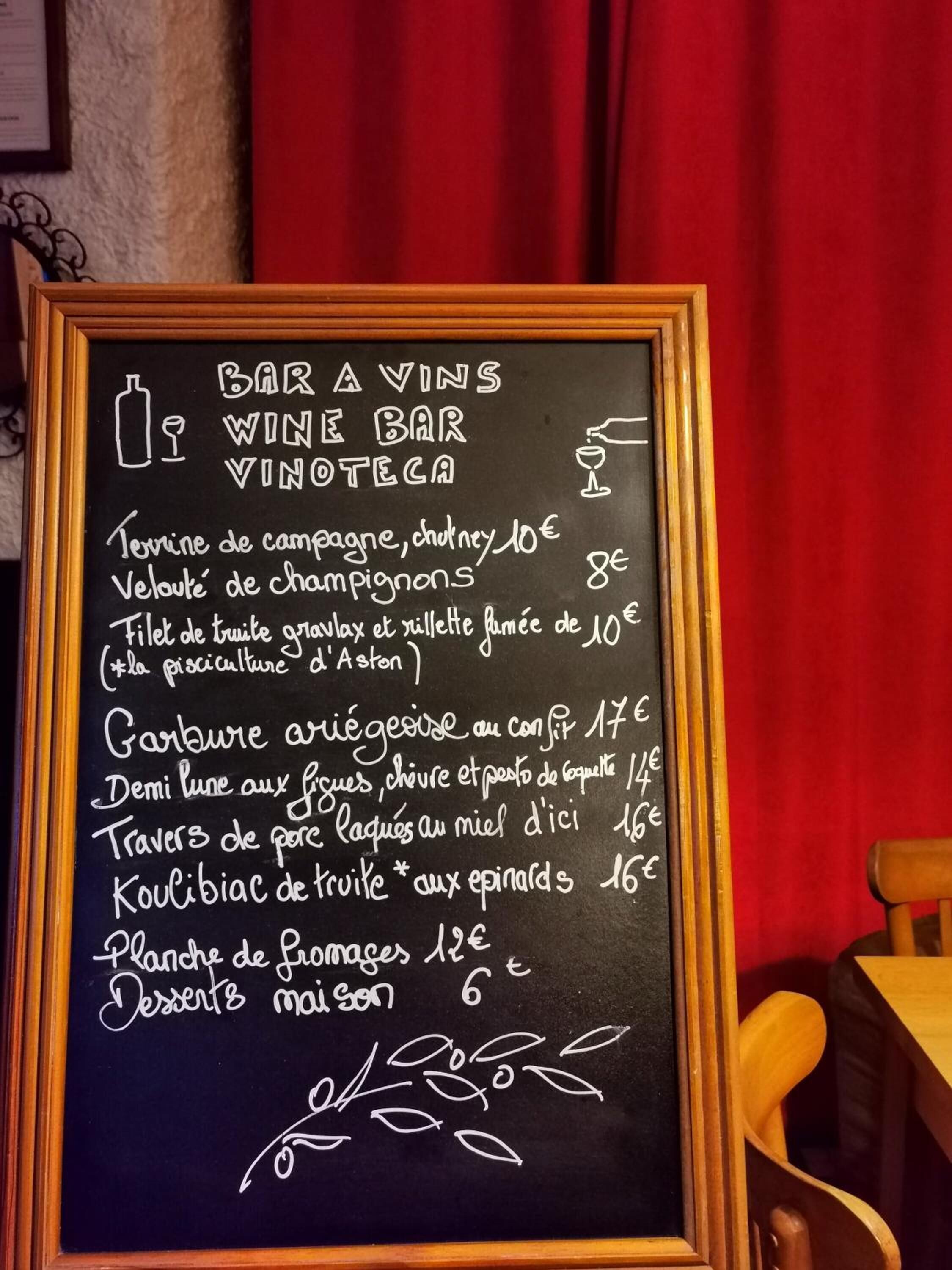 Una lavagna con il menu di un bar del vino che elenca diversi piatti e bevande con i relativi prezzi.
