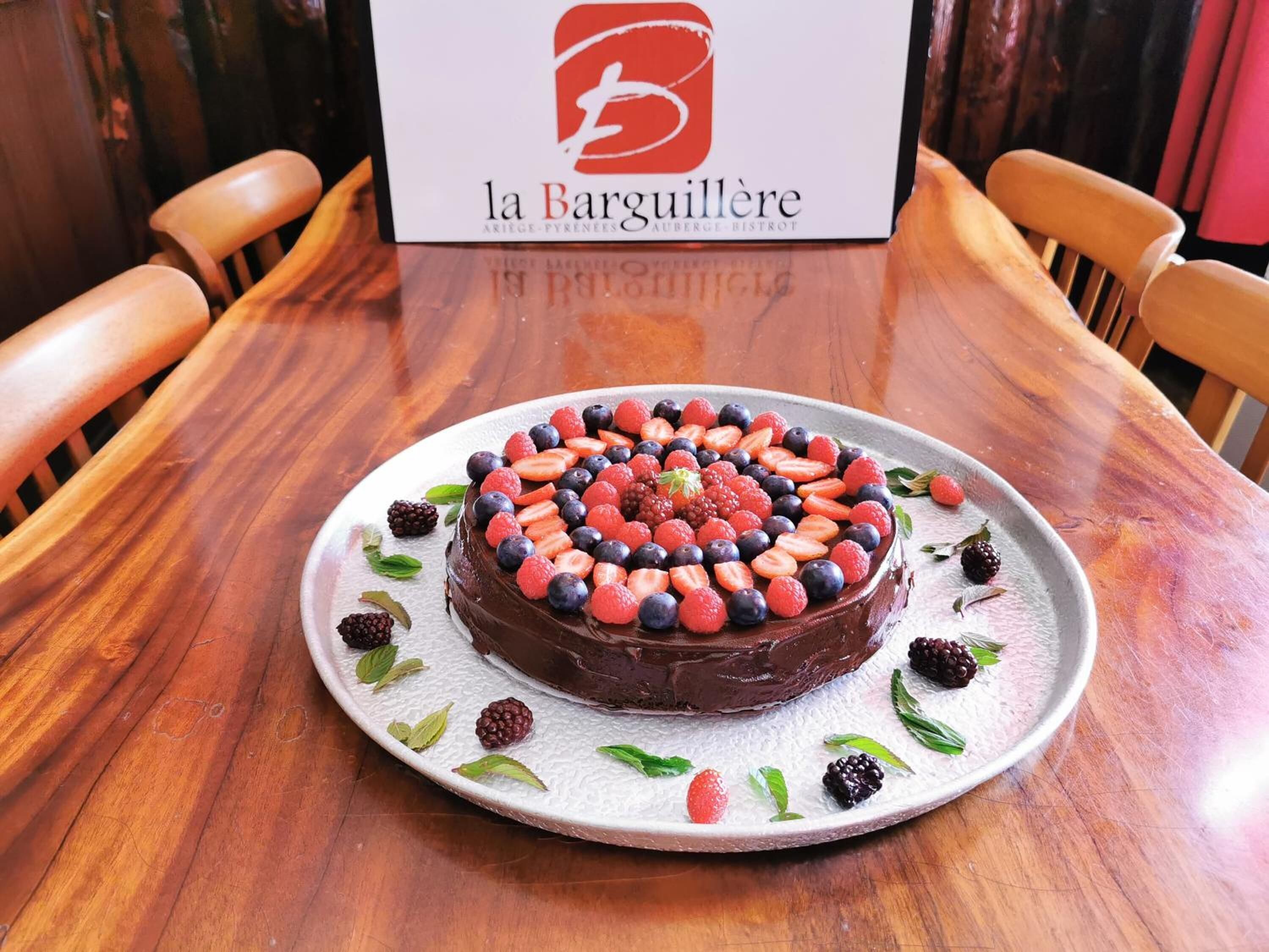 Chokoladekage med bær på en tallerken, med et skilt med teksten "la Barguillère" i baggrunden.