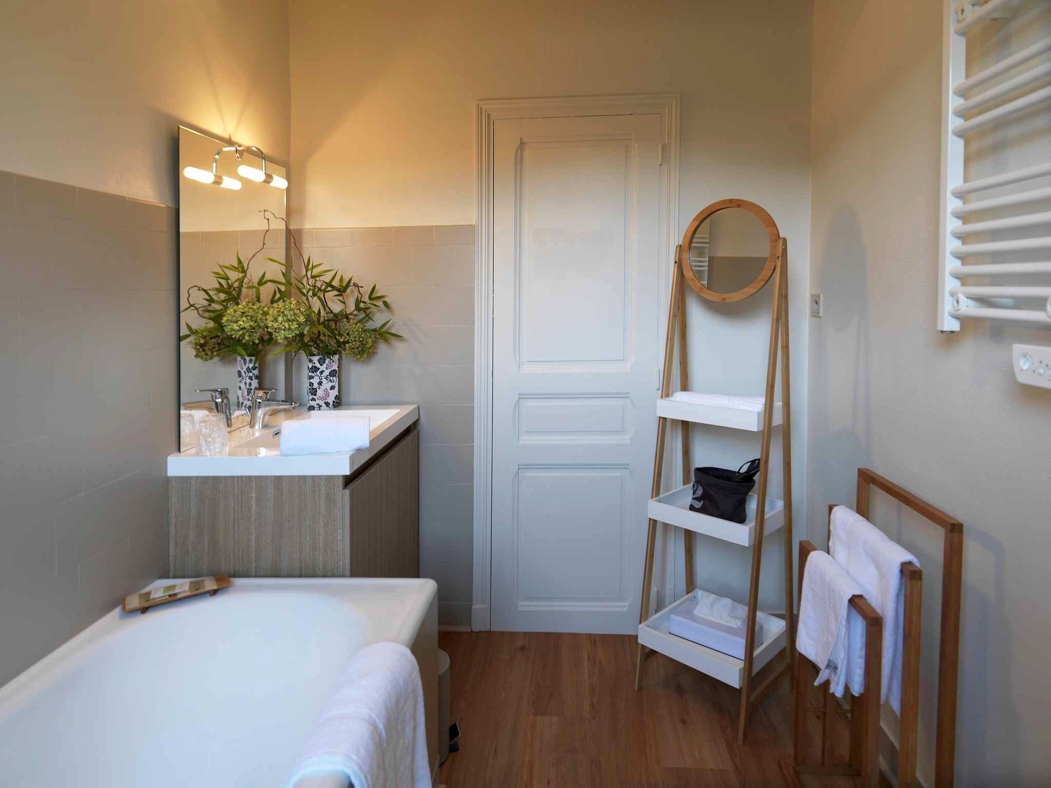 Un bagno con pavimento in legno, un lavandino bianco, uno specchio illuminato, una porta e uno scaffale con asciugamani.