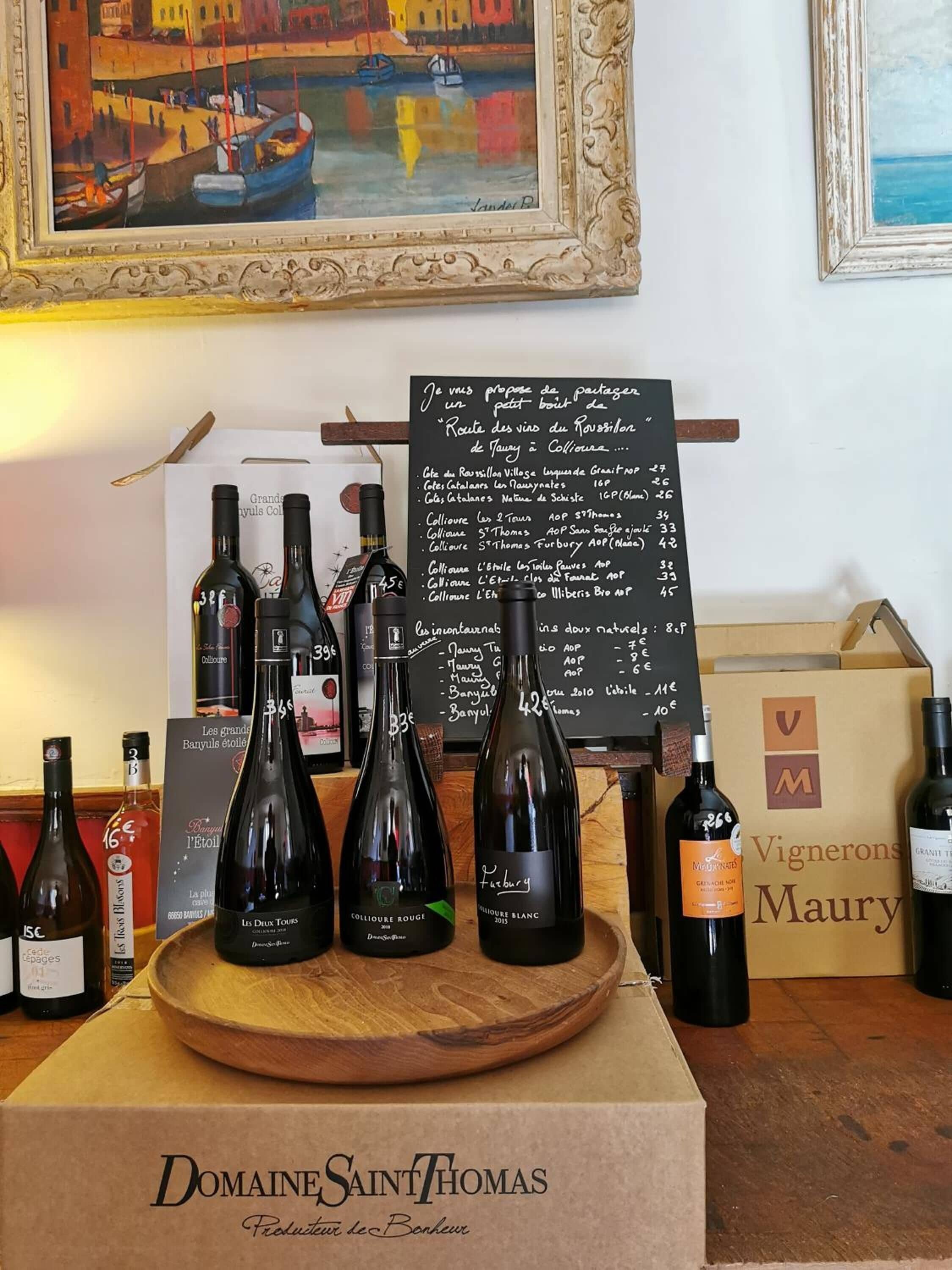 Una degustación de vinos con botellas sobre una tabla de madera, un panel con la carta y un cuadro enmarcado al fondo.