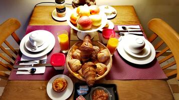 A breakfast table with plates of fruit, croissants, and a basket of bread.
