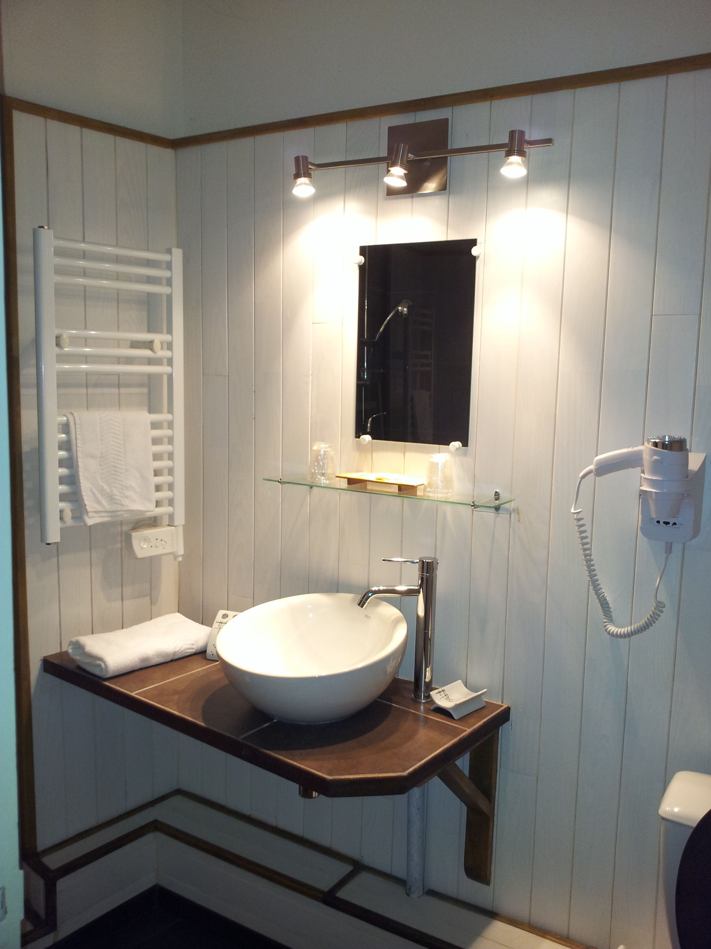 A bathroom with a white vessel sink, a mirror, a towel rack, and a glass shelf.
