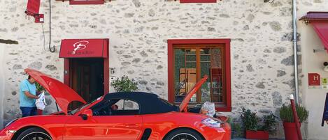 Un auto deportivo rojo estacionado frente a un edificio con fachada de piedra, contraventanas rojas y un letrero que dice 'la Barguillerie'.