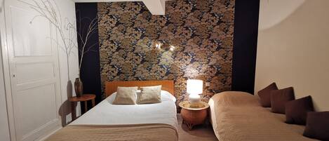 Une chambre avec deux lits, une table de chevet avec une lampe, un mur décoratif et une petite table avec un vase.