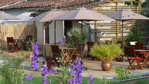Un espacio al aire libre con mesas y sillas de madera, sombrillas y plantas en macetas.