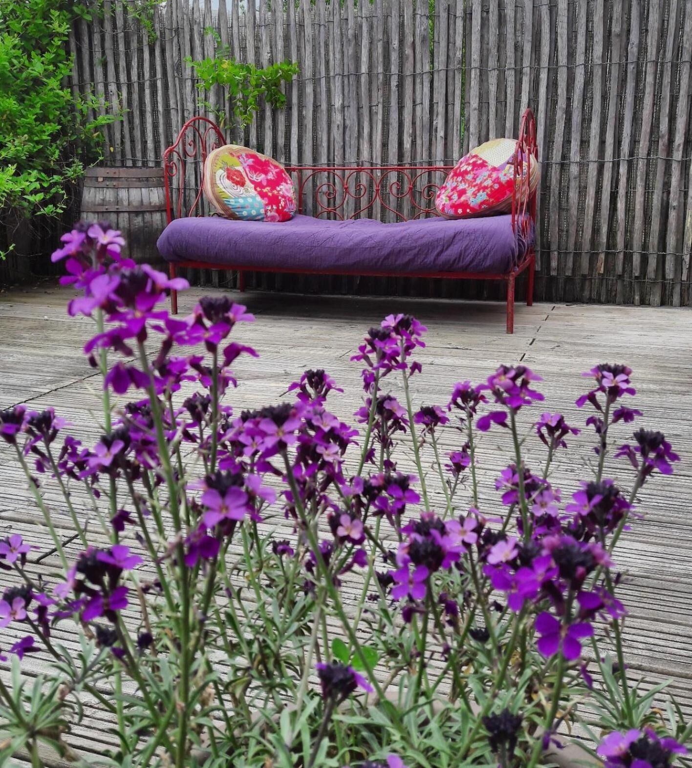 Una terraza de madera con un banco de metal y cojines morados.