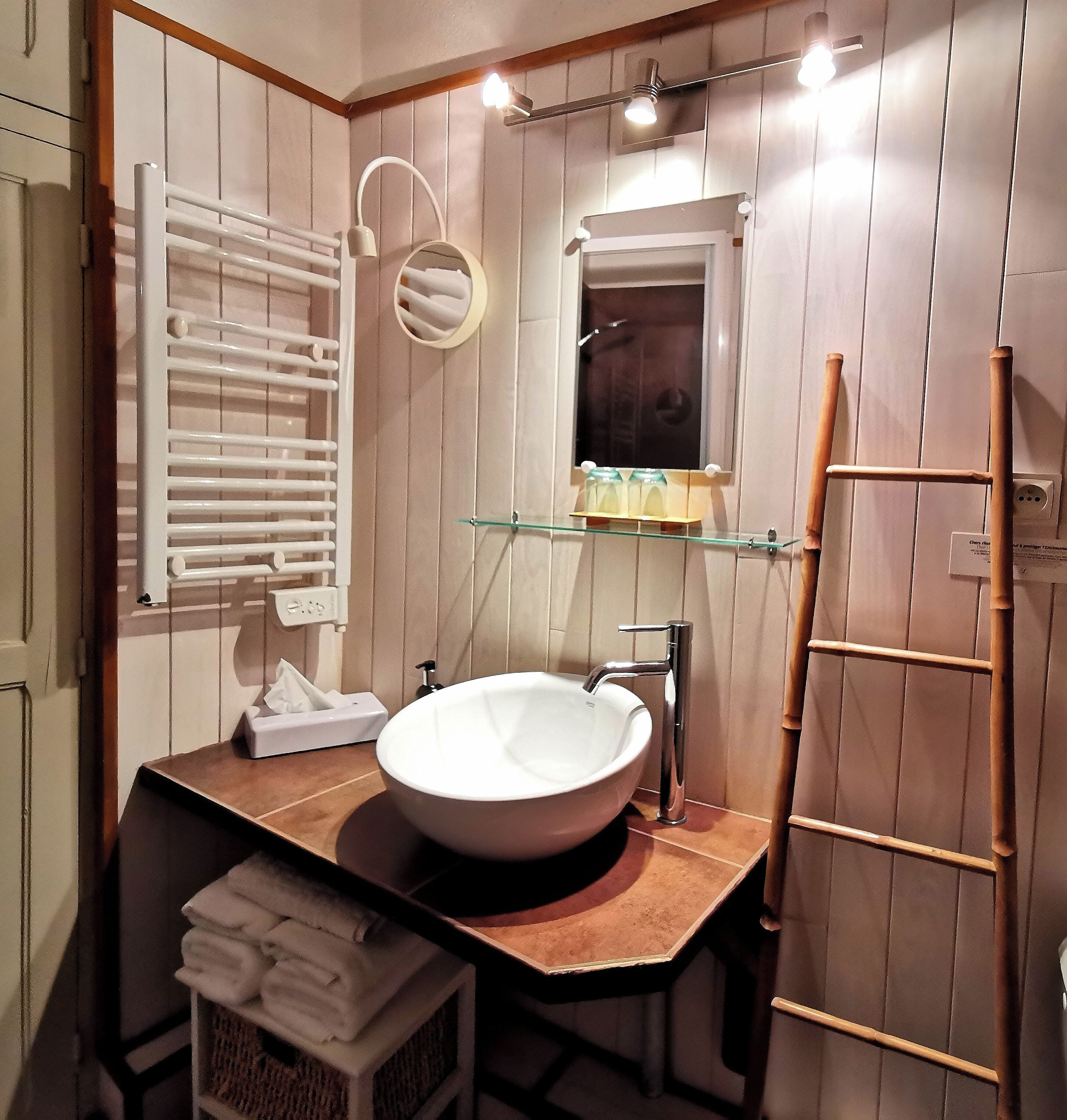 A bathroom with a white sink, a mirror, a towel rack, and a shelf with toiletries.