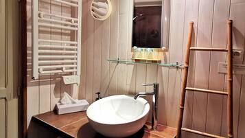 Un baño con un lavabo blanco, un espejo, un perchero para toallas y un estante con artículos de tocador.