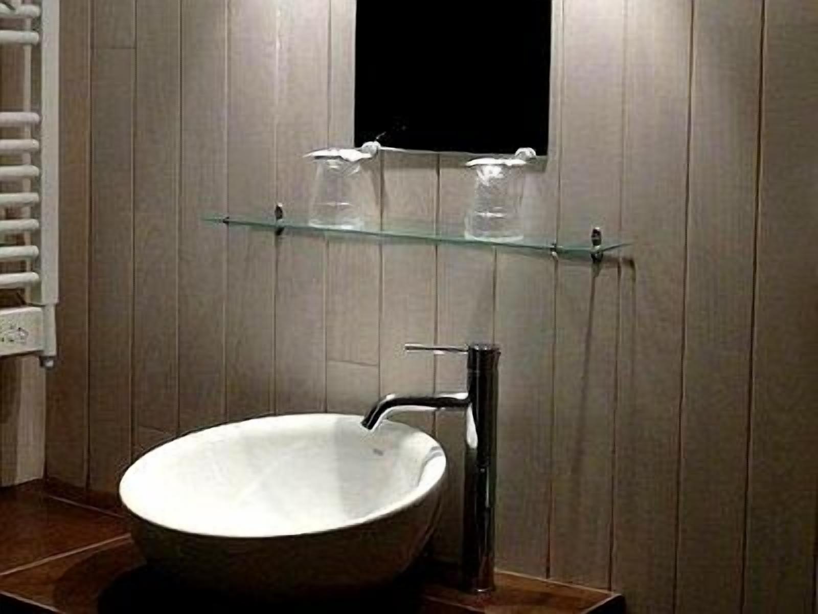 Een badkamer met een vrijstaand wastafel en een glazen plank erboven, plus een handdoekhouder aan de linkerkant.