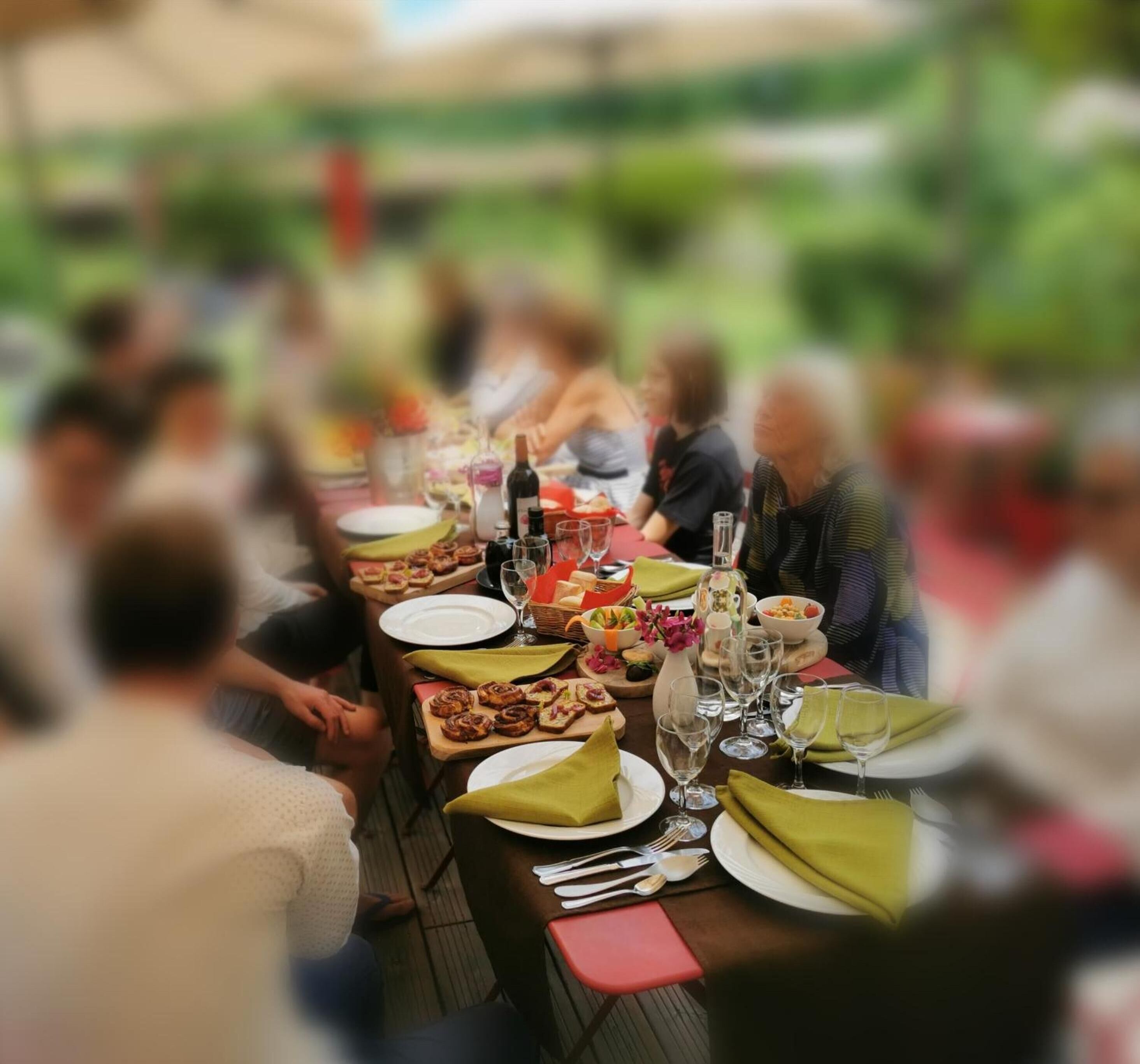 A dining table set with plates, glasses, and food items, surrounded by people.