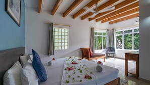 Una camera da letto con un letto, cuscini, una panca, una sedia, un tavolo e vista sul verde.